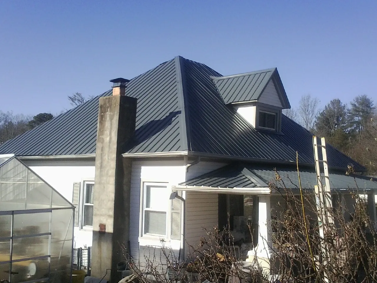 Dark blue standing seam metal roof on a white farmhouse with dormer — Slate & Tile Roof Repair by Roofing Brothers in Kouts