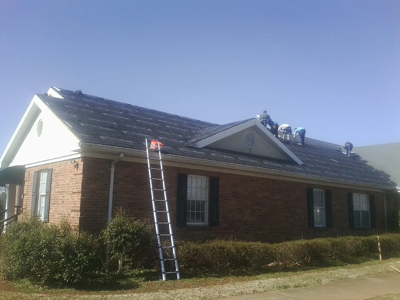 Crew tearing shingles off a brick ranch roof with a ladder set — Metal Roof Repair work by our crew in Kouts