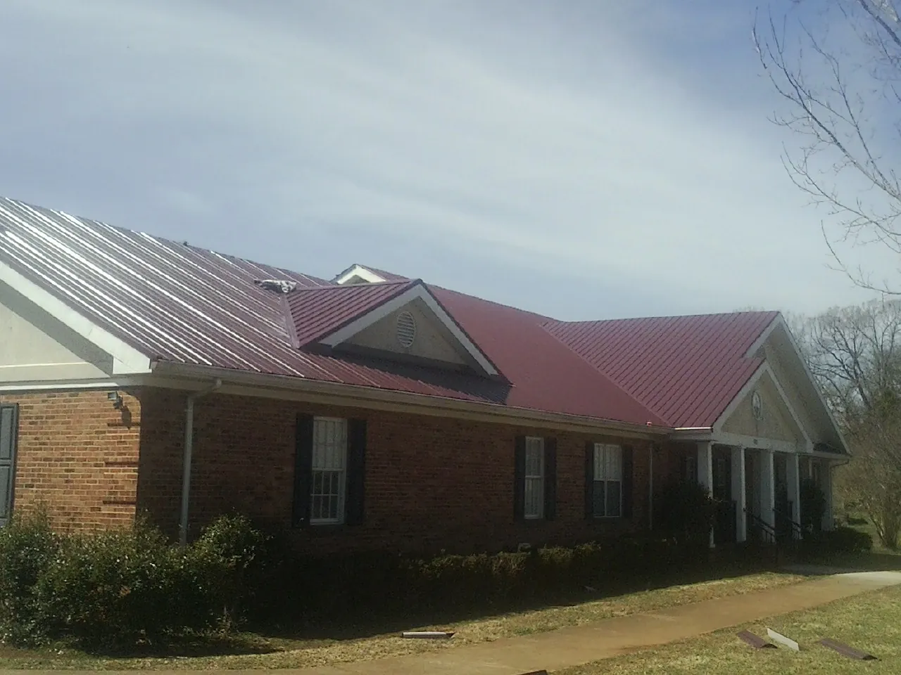 Red metal roof with gabled entries on a long brick building, from a Hail Damage Roof Repair job in Kouts