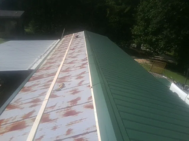Old rusted panels beside newly installed green metal roofing — Wind Damage Roof Repair by Roofing Brothers in Kouts