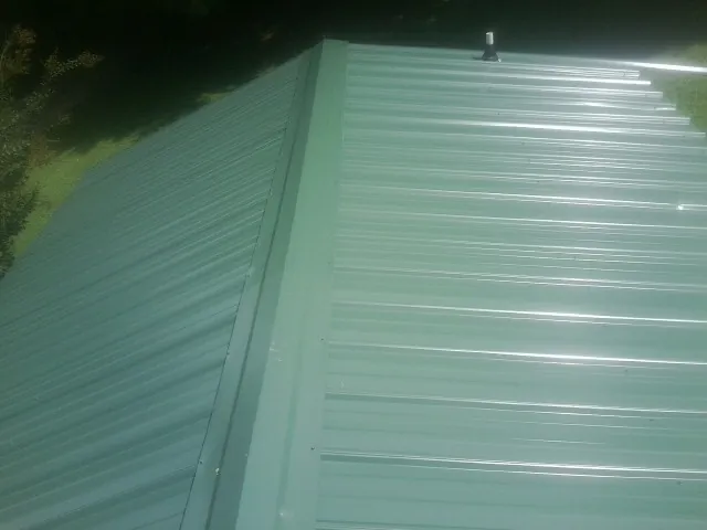 New green metal panels meeting at the ridge of a roof — Flat Roof Repair work by our crew in Kouts