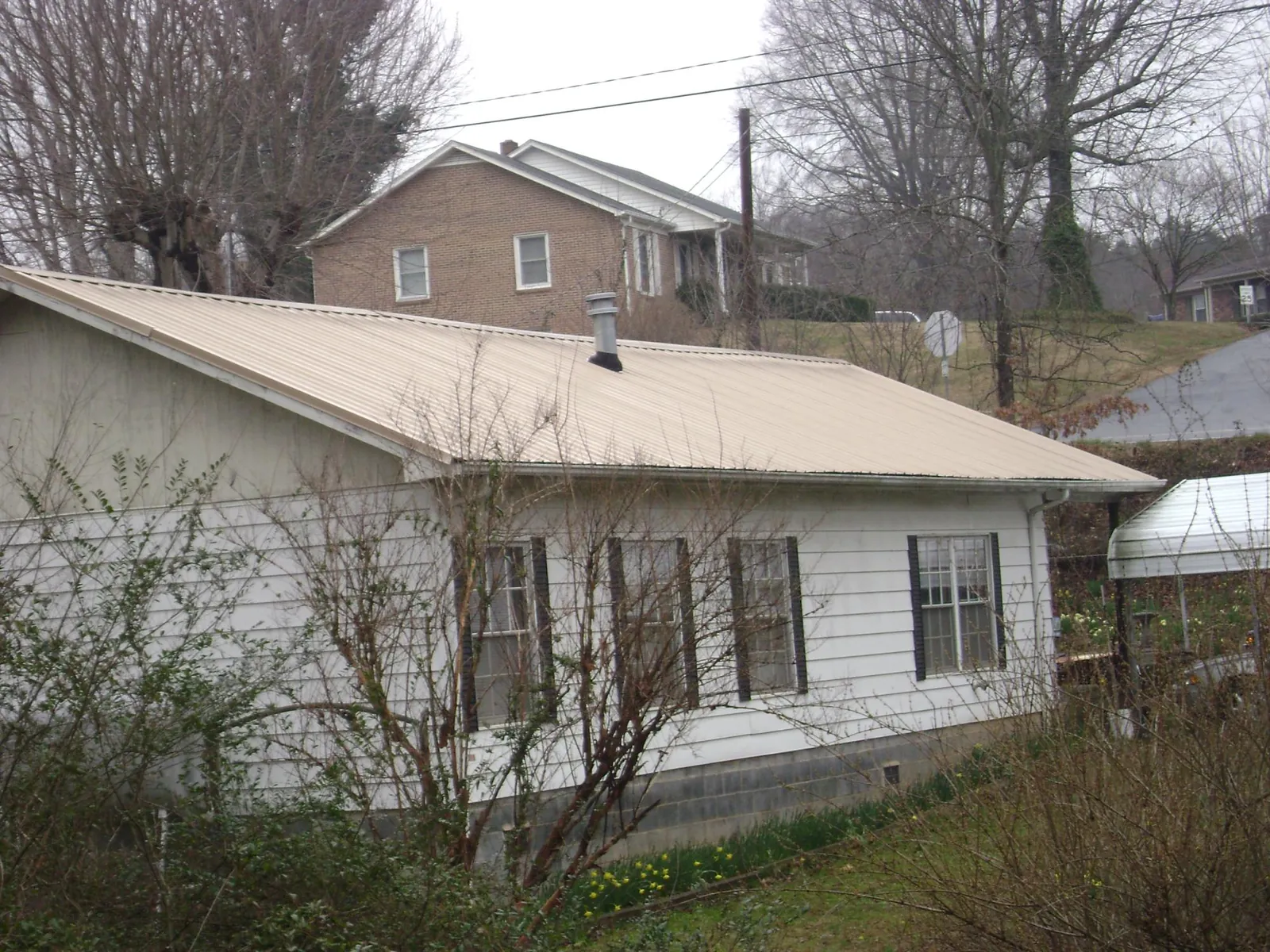 Tan metal roof on a white sided house set into a hillside — Commercial Roofing by Roofing Brothers in Kouts