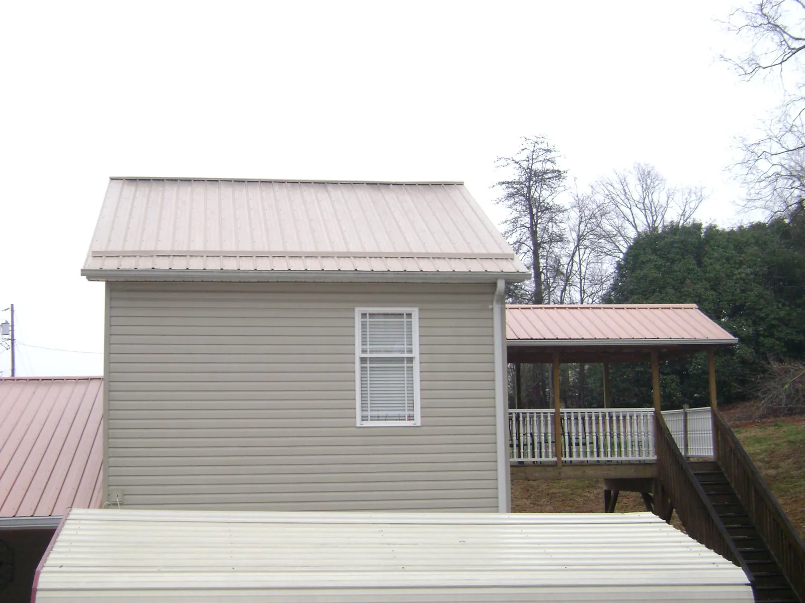 Tan metal roofs on a two story addition and attached porch, from a Roof Replacement job in Kouts